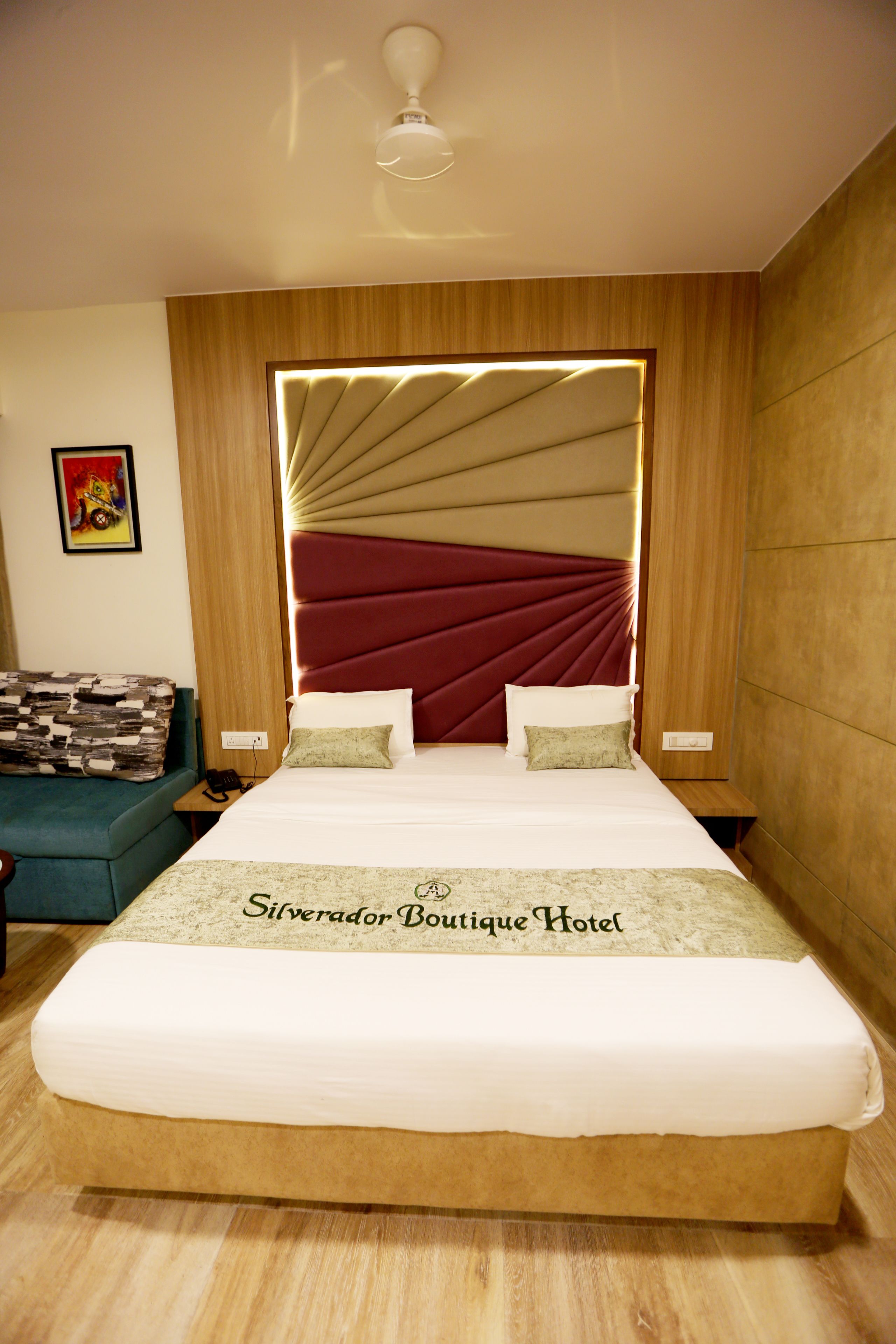 Een hotelkamer met een groot bed, een hoofdeinde met een verlicht paneel, een kleine tafel, een nachtkastje en een bank.