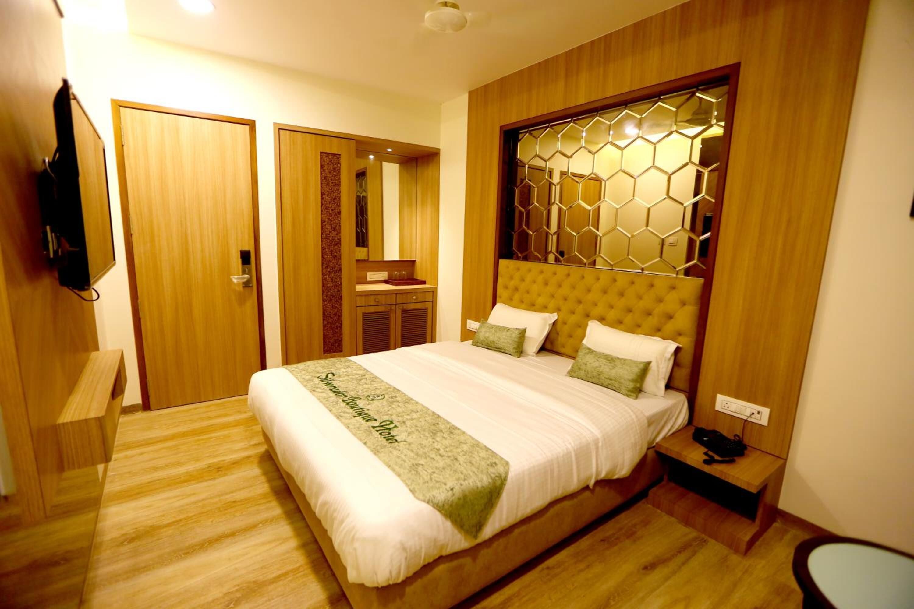 A modern hotel room with a large bed, wooden paneling, a decorative headboard, and a small bedside table.