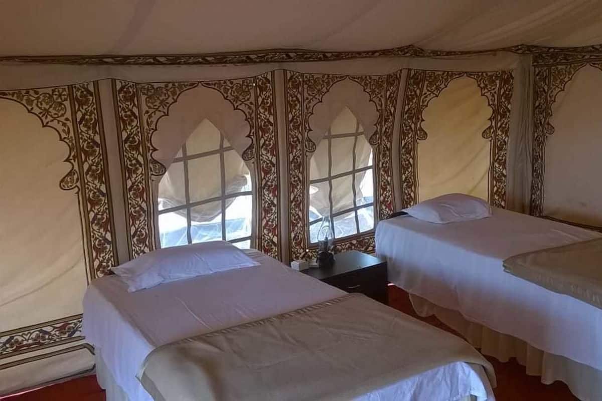 A tent-style room with two beds, each with white linens and a small bedside table.