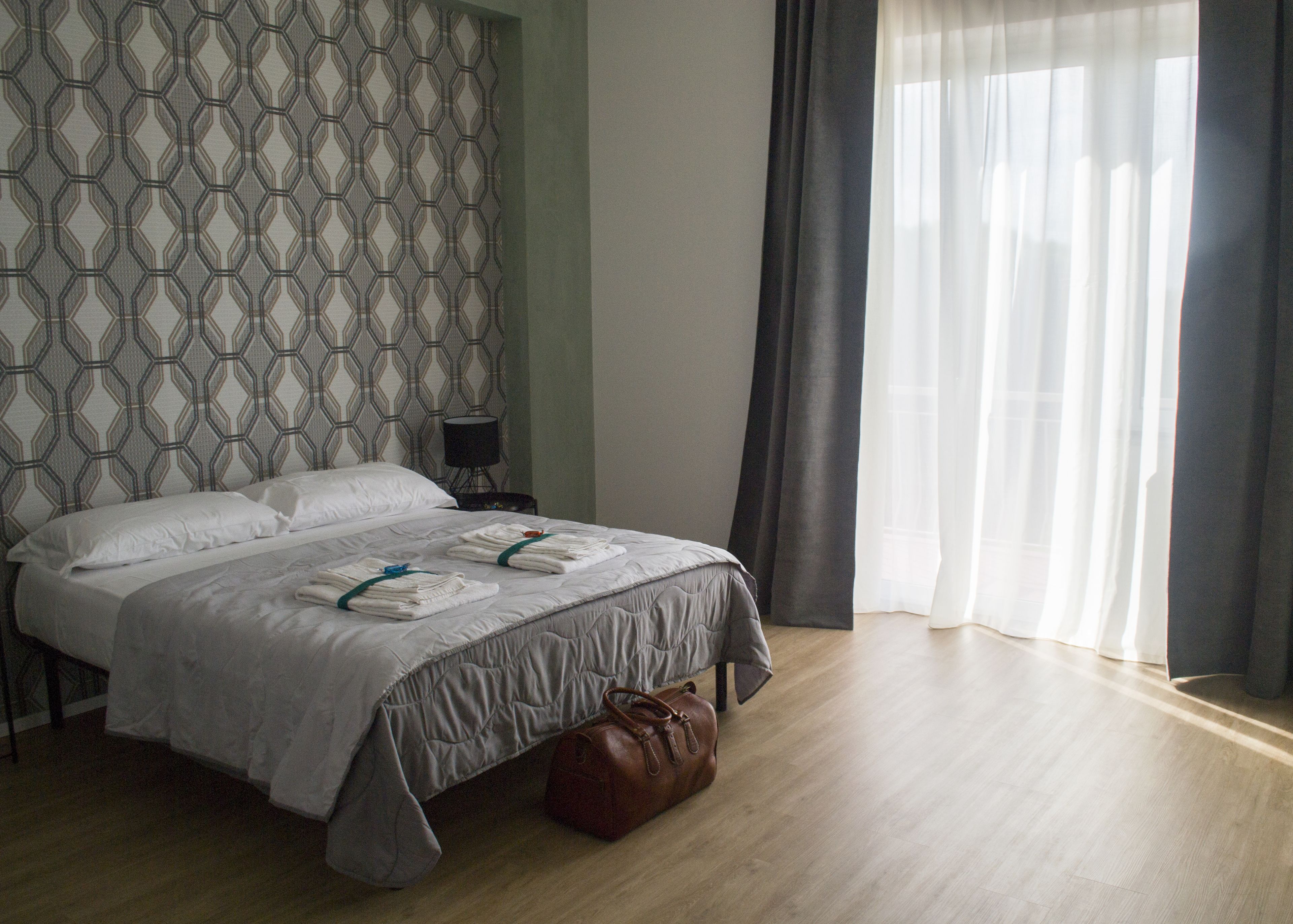 A neatly made bed with white linens and a brown leather bag on the floor.