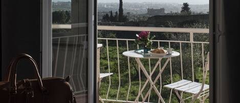 A balcony with a view of a cityscape, a table with a vase of flowers, and a handbag on the floor.