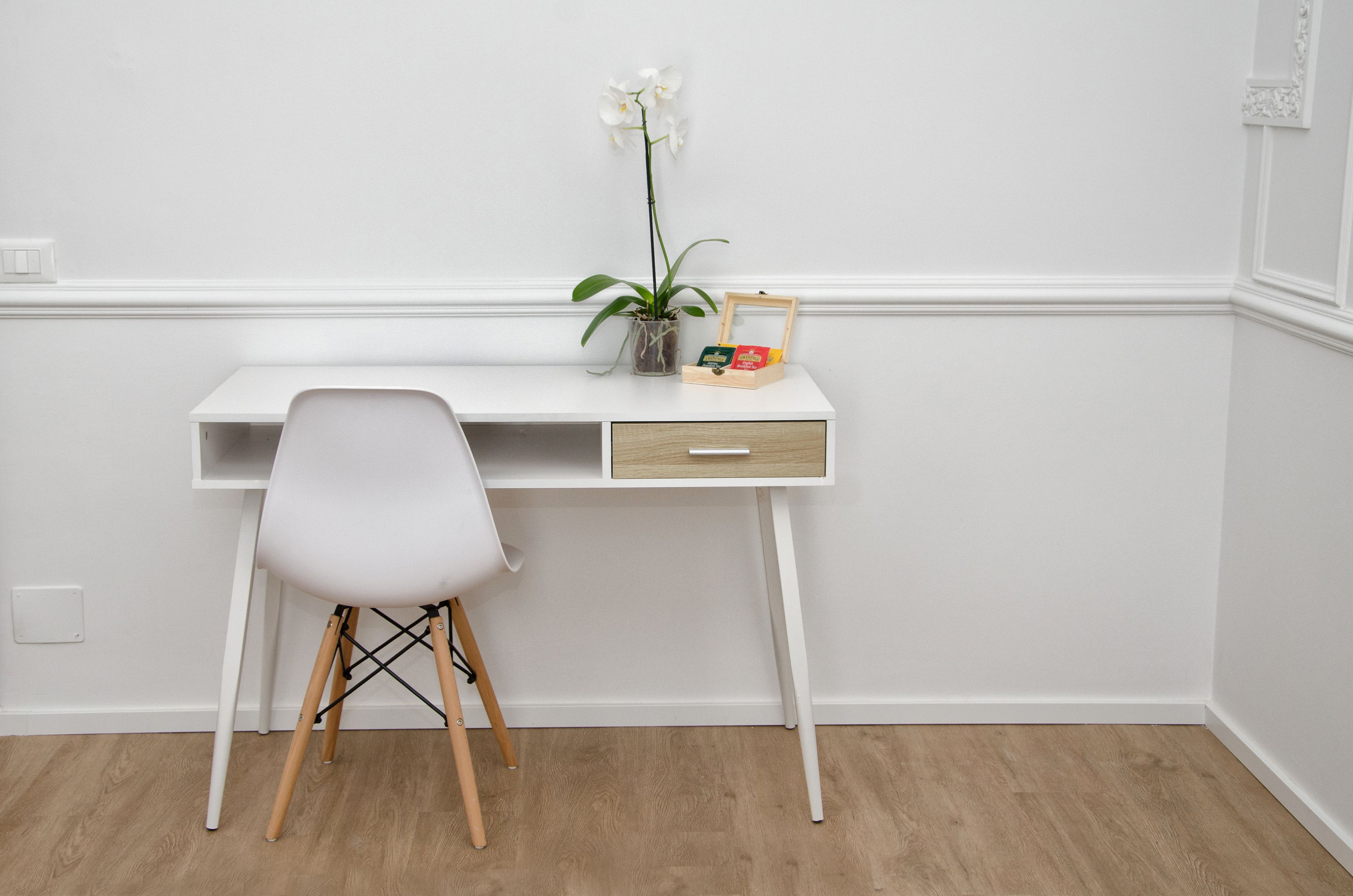 Un bureau blanc avec un tiroir, une chaise blanche, une orchidée en pot et une petite boîte en bois.