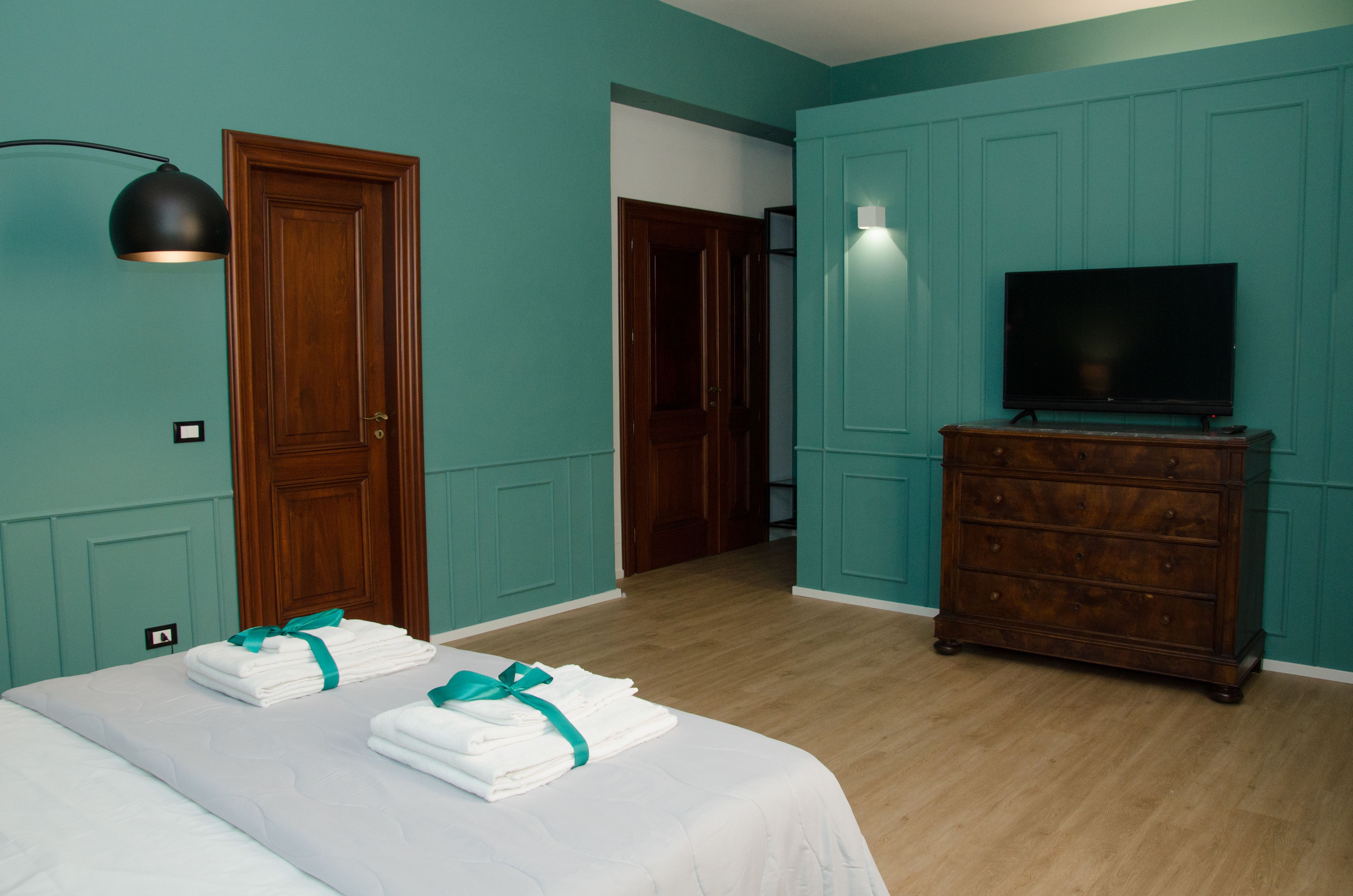 A hotel room with teal walls, a wooden door, a TV on a dresser, and two beds with folded white towels.