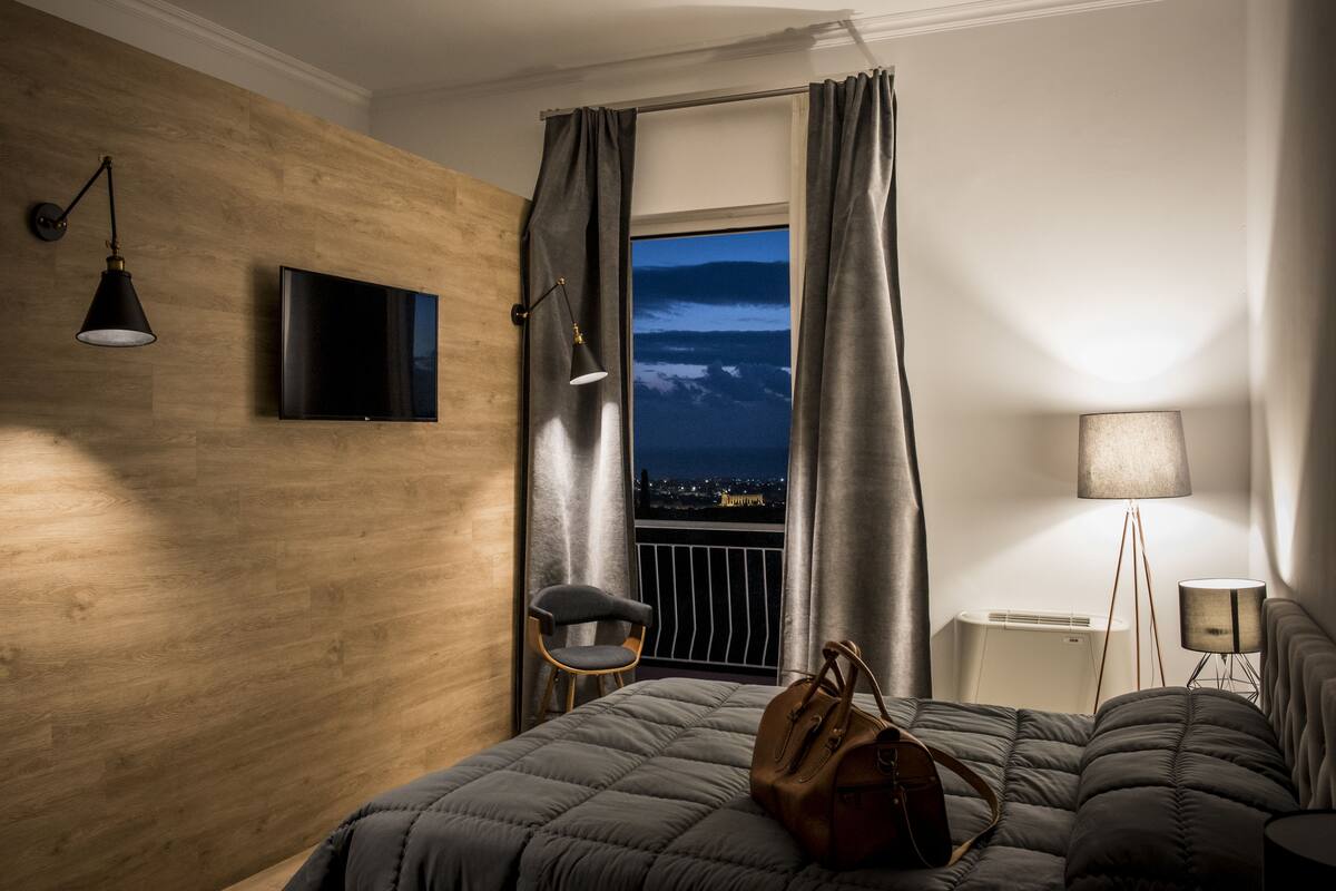 Una habitación de hotel con una cama, una silla, un televisor, una ventana con cortinas y una lámpara.