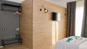 Ein modernes Hotelzimmer mit einer Wand in Holzoptik, einem Bett mit ordentlich gefalteten weißen Handtüchern, einem an der Wand montierten Fernseher und einer Pendelleuchte.