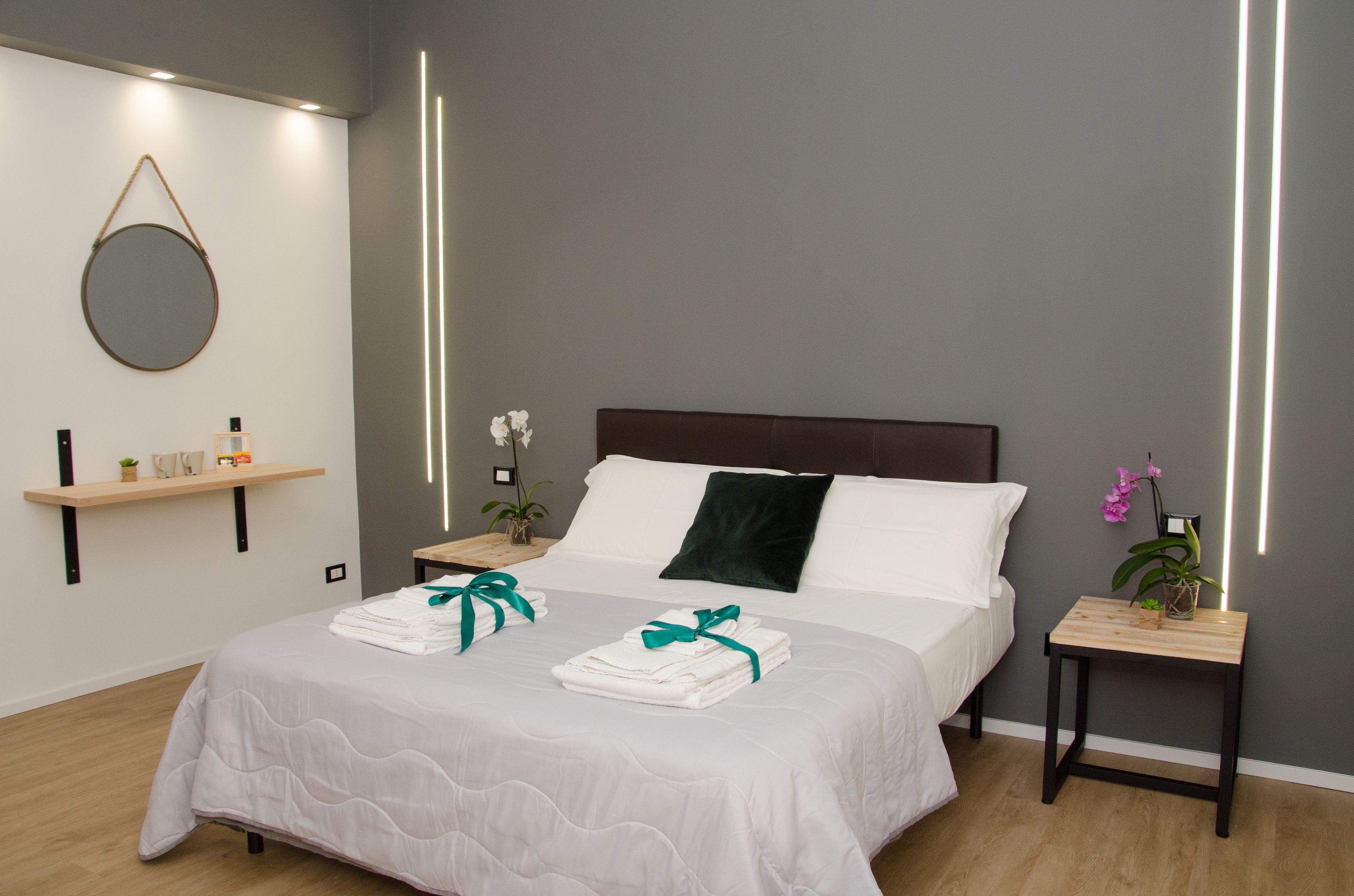 A neatly made bed with white linens and teal ties, a dark headboard, and a bedside table with a plant.