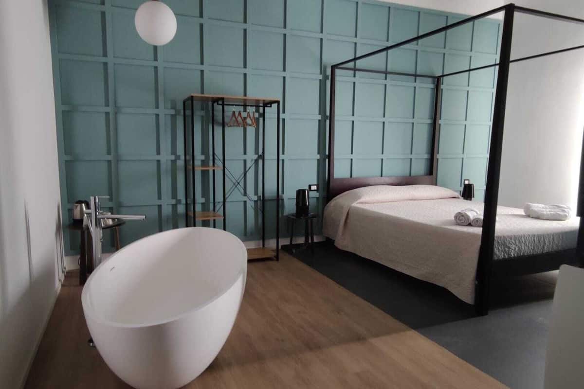 Un dormitorio moderno con una cama con dosel, una bañera blanca grande y una zona de ducha con paredes de vidrio.