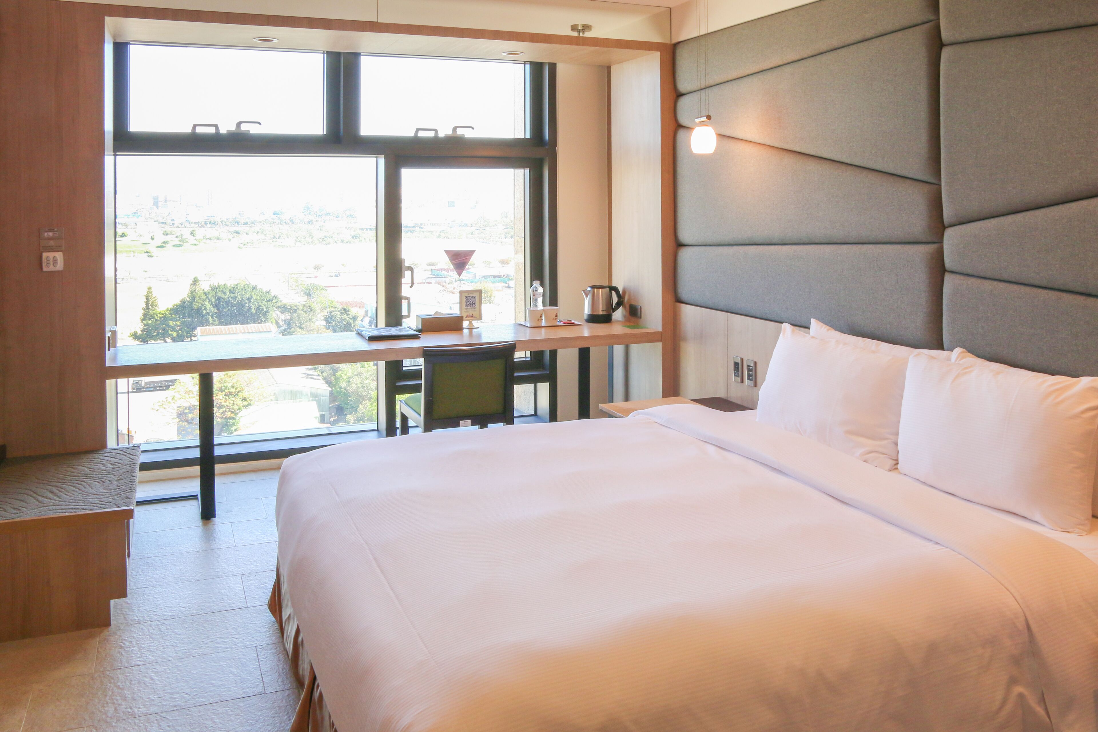 Habitación de hotel con una cama grande, un escritorio con silla, una ventana con vistas y un cabecero acolchado.
