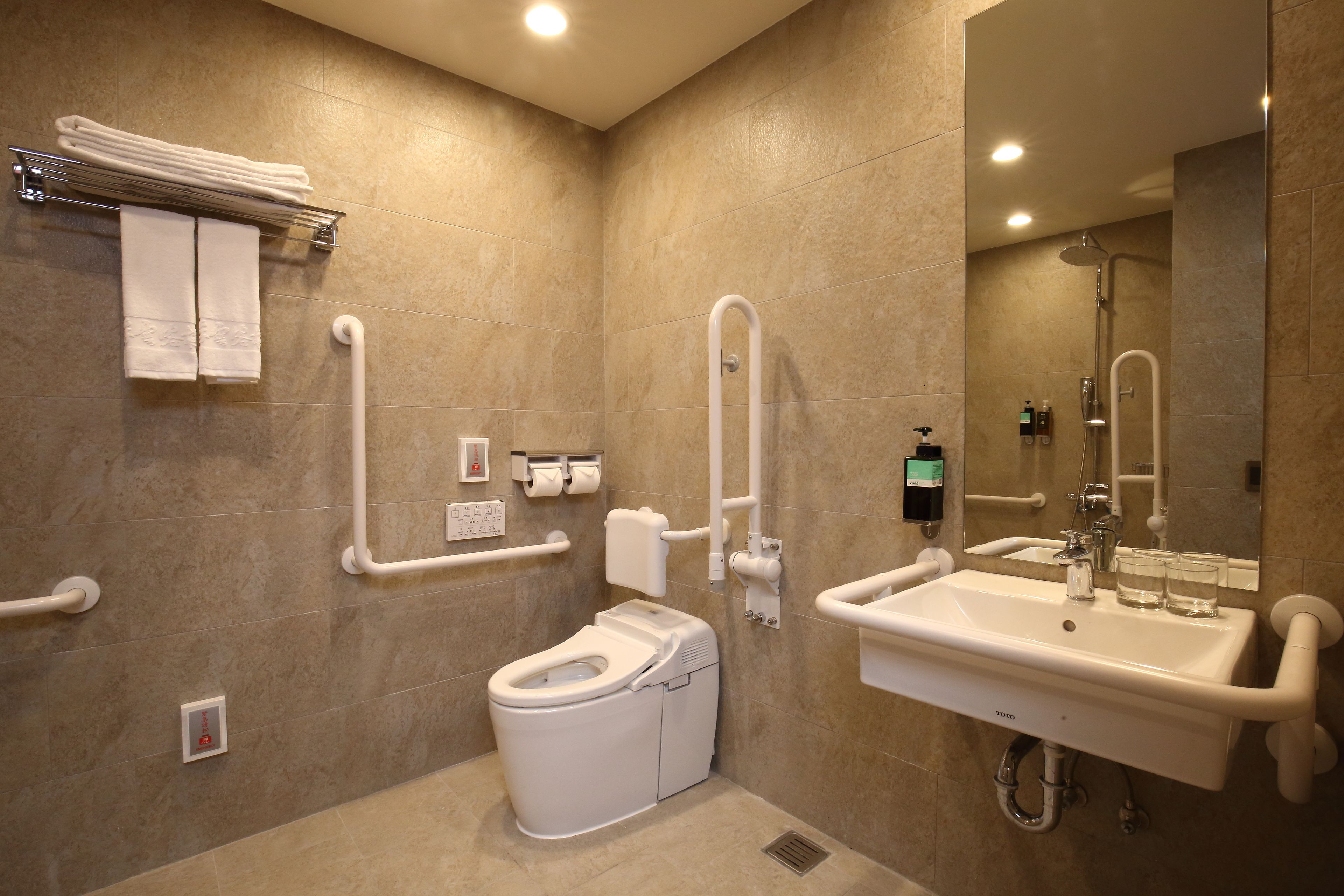 Une salle de bain moderne équipée de toilettes, d’un lavabo et d’une douche. Elle comprend également des barres d’appui et un sèche-mains.