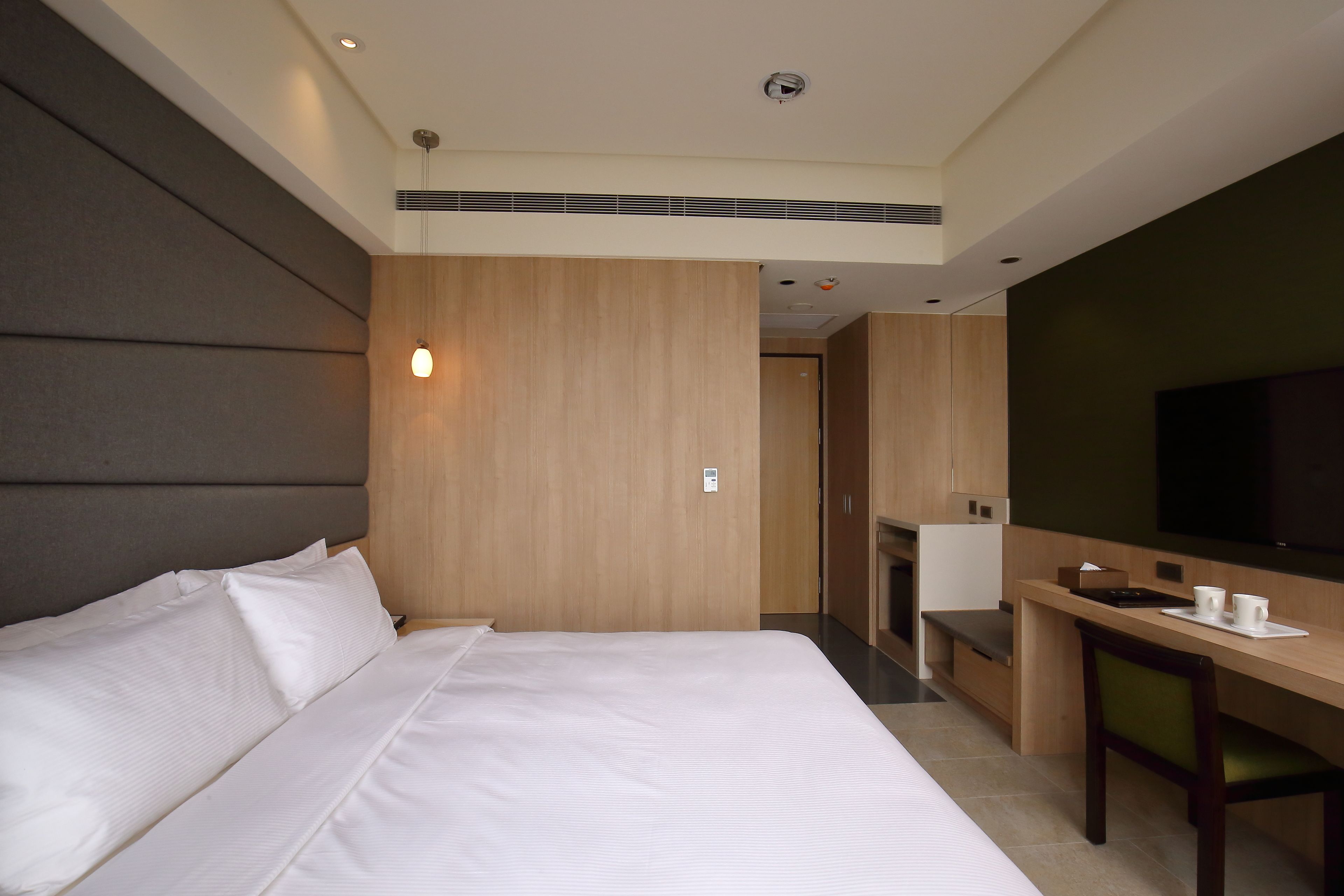 A hotel room with a bed, a desk, a chair, a television, and a small kitchenette.