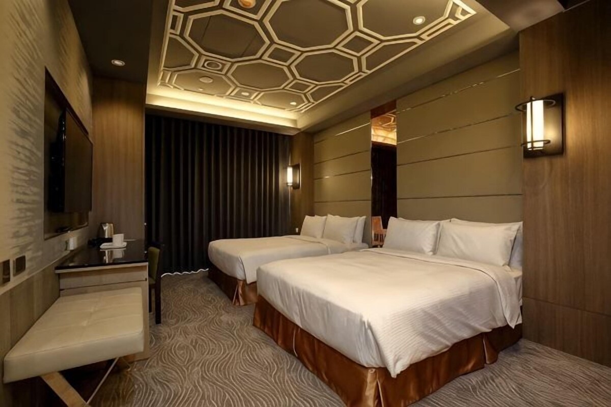 Habitación de hotel con dos camas, un escritorio, una silla, un espejo grande y un diseño de techo singular.