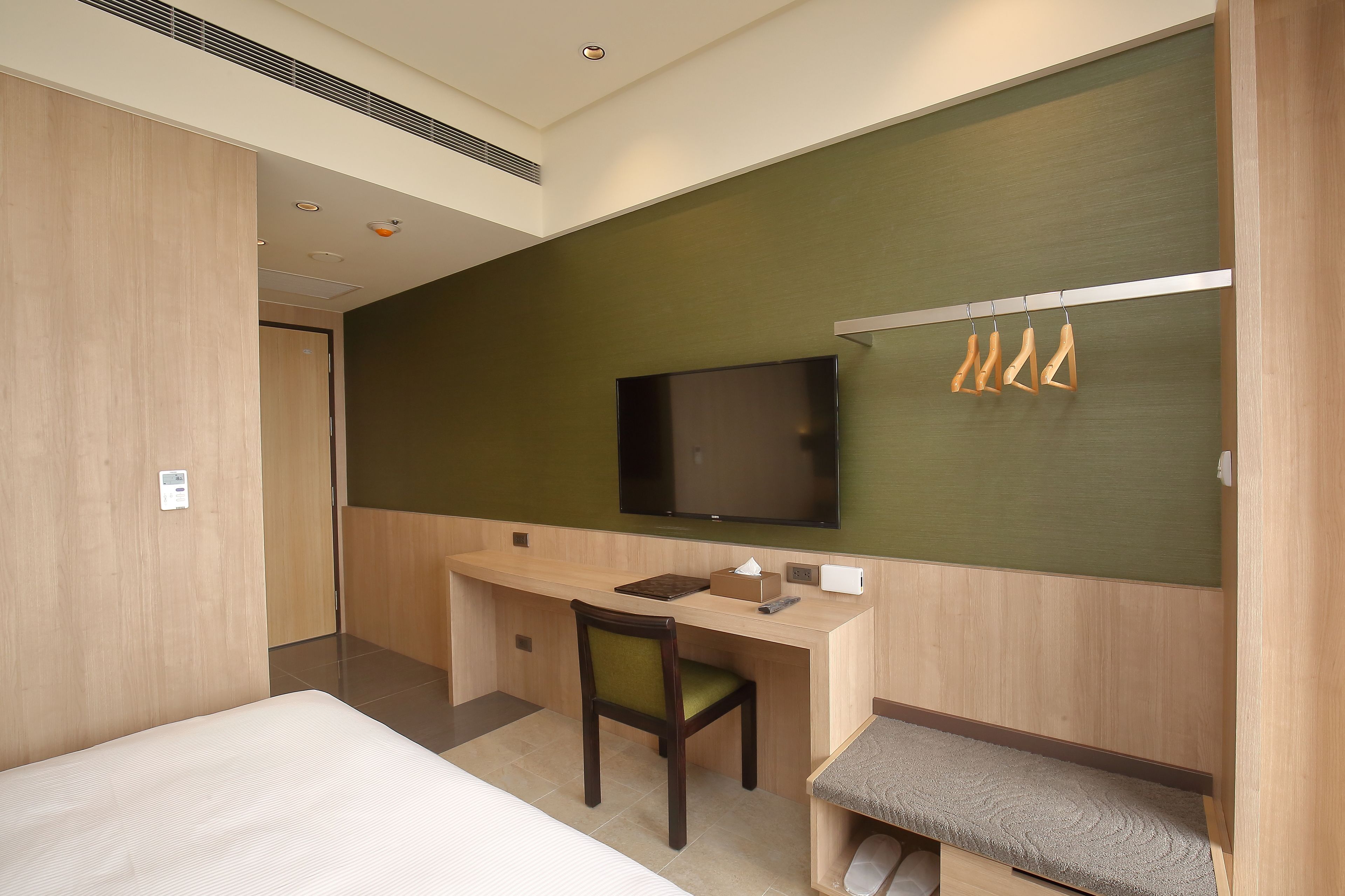Una habitación de hotel con cama, escritorio con silla, televisor y zapatero.