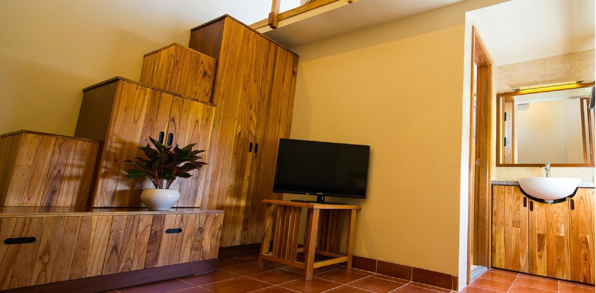 Een houten kast met een televisie op een standaard, een potplant en een badkamer met een wastafel en spiegel.