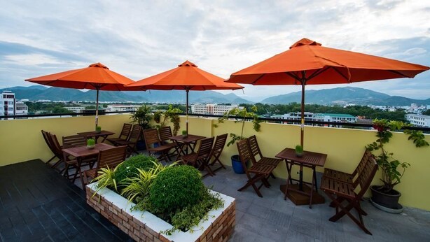 Terraza en la azotea con mesas y sillas de madera, sombrillas naranjas y plantas en macetas.