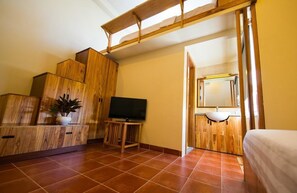 A bedroom with a wooden wardrobe, a television on a wooden stand, a potted plant, and a bathroom with a sink and mirror. - Tabalo Hostel (Nha Trang)