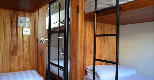 Dormitorio con literas, paredes de madera, una puerta con pomo y un interruptor de luz en la pared.