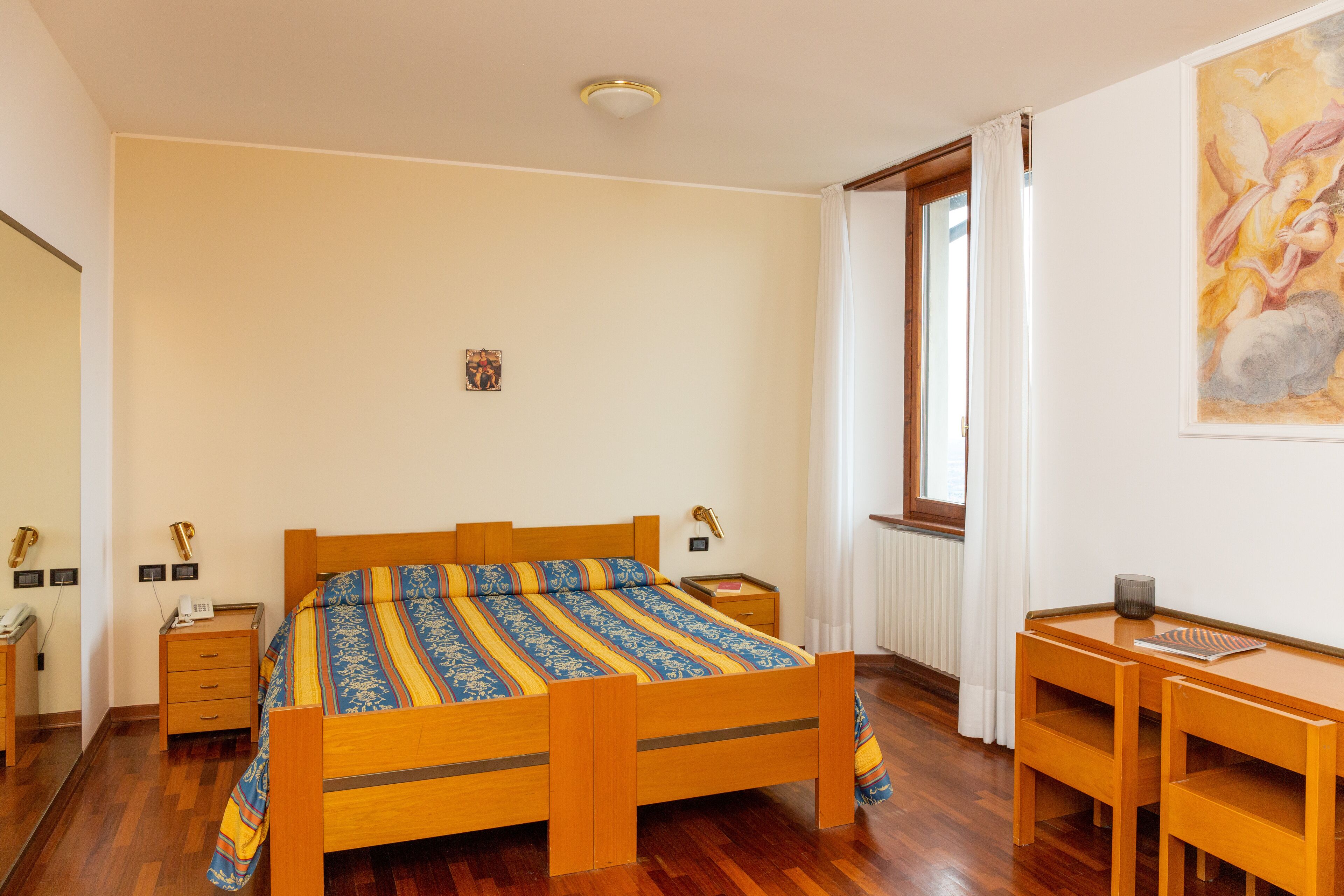 A bedroom with a wooden bed, bedside tables, a desk, and a chair.
