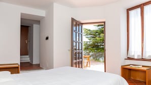 A bedroom with a large bed, a wooden nightstand, a chair, and a window with curtains. - Albergo Sacro Monte Varese (Varese)