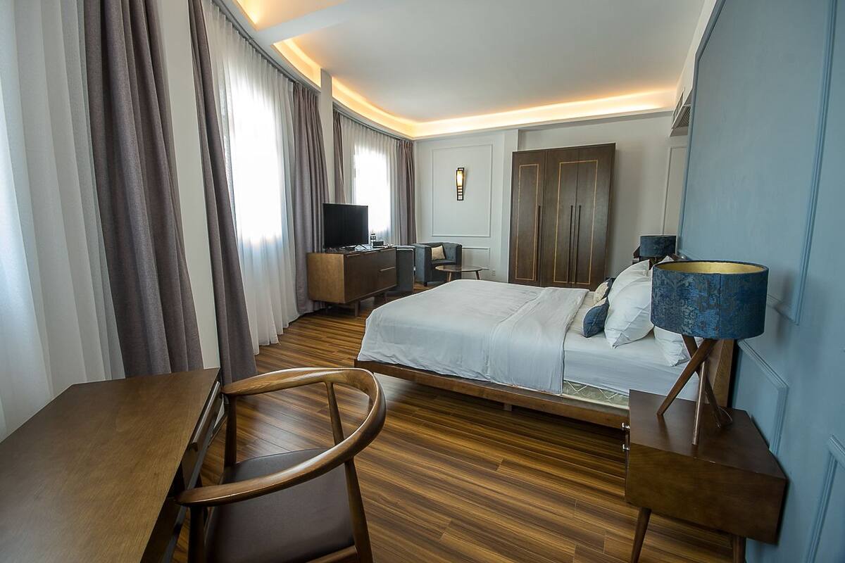Una habitación de hotel con cama, escritorio, silla, televisor y lámpara.