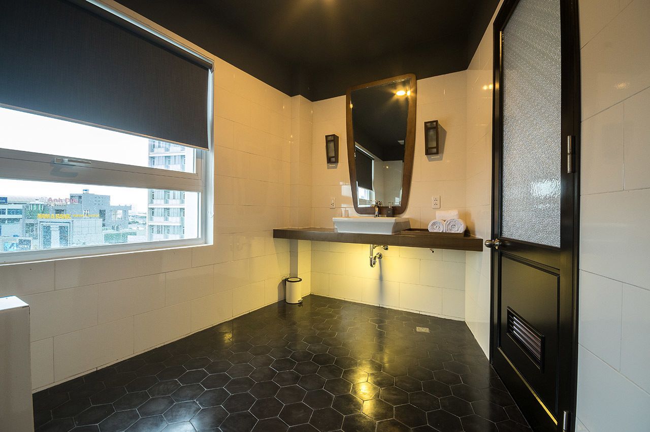 A modern bathroom with a large window, a black hexagonal floor, a white sink, and a mirror above it.