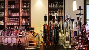 A bar area with various bottles of alcohol, glasses, and a candle holder. - Restaurant Esslust (Niedergoersdorf)