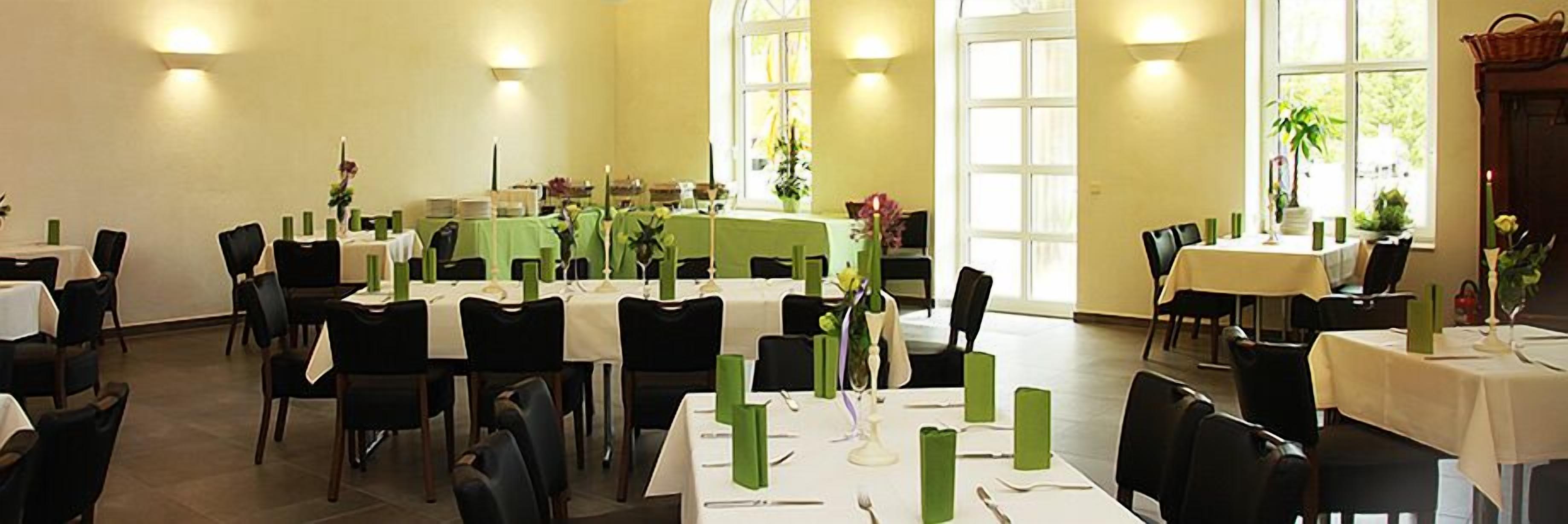 Un espace repas avec plusieurs tables dressées pour accueillir les convives, agrémenté de serviettes vertes et de nappes blanches.