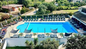 Une grande piscine, dotée de chaises longues et de parasols, entourée de verdure et de quelques bâtiments.
