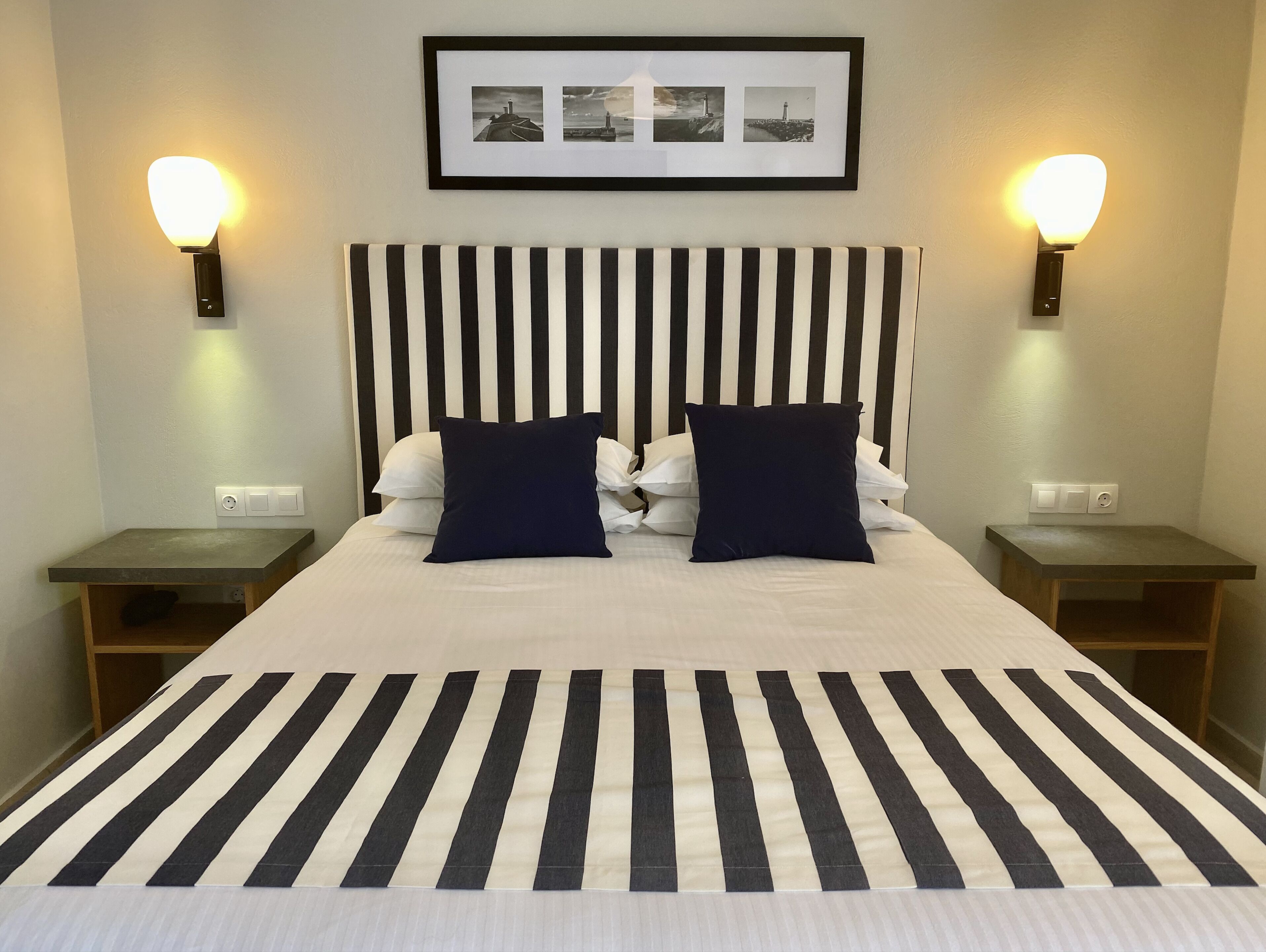 A hotel room with a striped bedspread, a black and white striped headboard, and two wall-mounted nightstands with lamps.