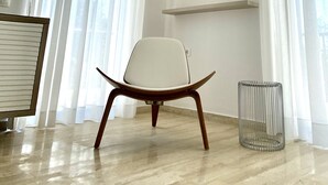 Une pièce moderne et bien éclairée, au design minimaliste, comprenant une chaise blanche, un petit radiateur en métal et un téléviseur fixé au mur.
