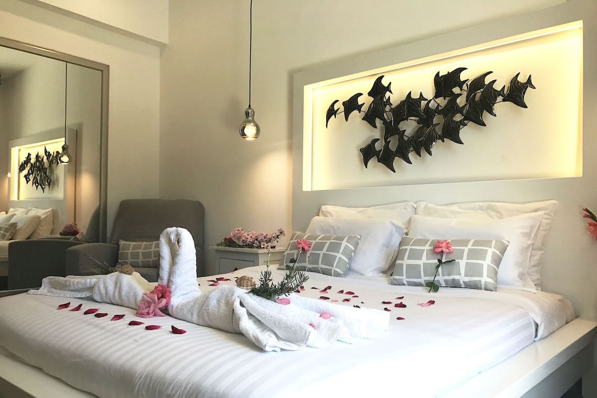 Ein ordentlich bezogenes Bett mit Rosenblättern, eine an der Wand befestigte Fledermaus-Dekoration und ein Spiegel, der den Raum reflektiert.