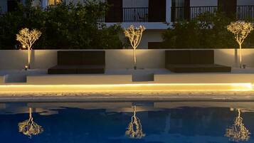 Zona de piscina con árboles iluminados y un reflejo en el agua.