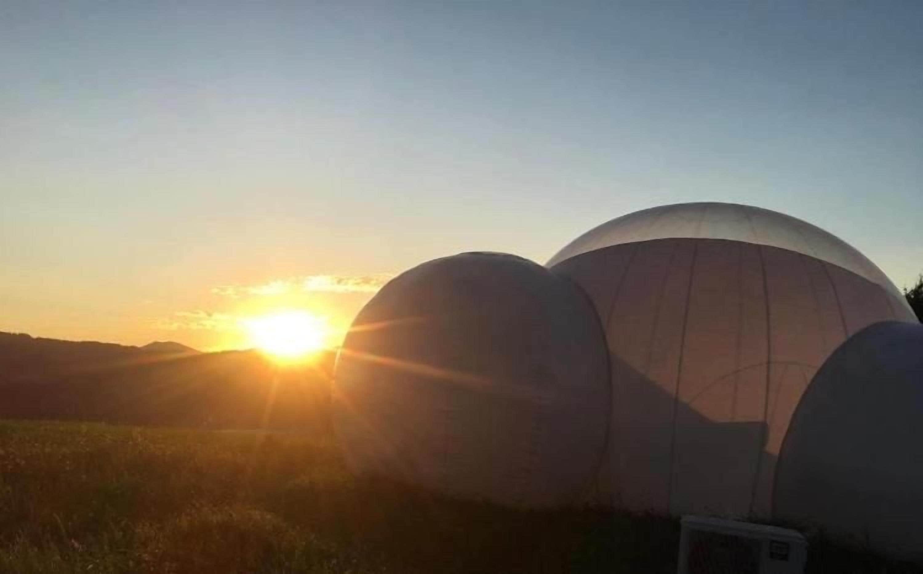 A dome-shaped structure with a clear sky and sun in the background.