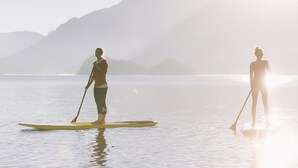 Due persone che fanno paddleboard su un lago calmo, con montagne sullo sfondo.