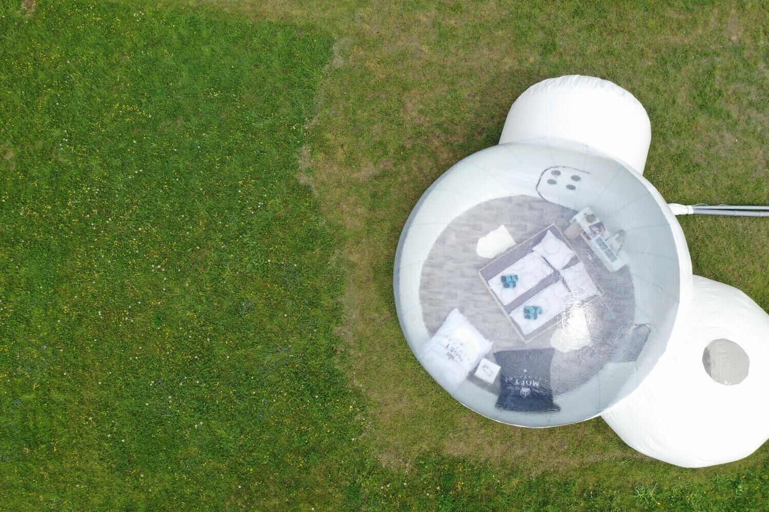 Vista aérea de una estructura inflable blanca con un área de visualización circular, posiblemente una carpa o refugio temporal, sobre un campo cubierto de hierba.