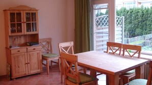 Un comedor con una mesa y sillas de madera, un armario con puertas de vidrio y vistas a un jardín por la ventana.