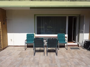 An outdoor patio with two green chairs and a table, a sliding glass door, and a brick wall.