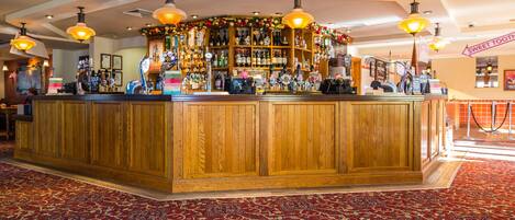 A bar area with wooden paneling, a variety of bottles, and a red patterned carpet.