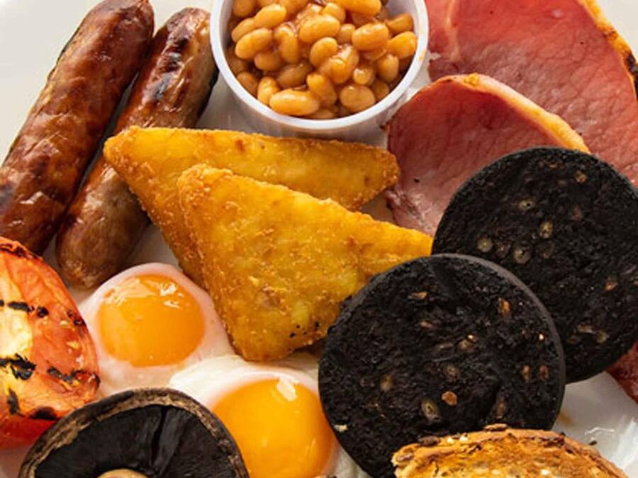 A plate of breakfast items including sausages, beans, ham, eggs, toast, and black pudding.