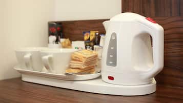 Una tetera eléctrica blanca sobre una bandeja con tazas y un pan tostado apilado.