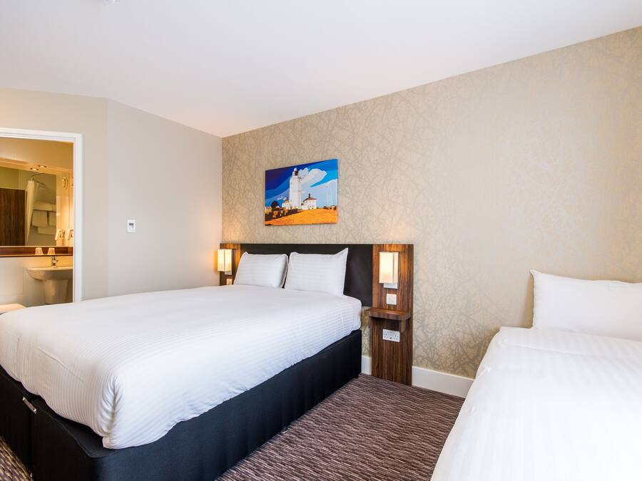 Ein Hotelzimmer mit einem großen Bett, einem kleineren Bett, einem Gemälde an der Wand und einem durchgegangenen Tür erkennbaren Badezimmer.