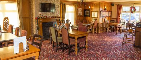 A spacious room with a large wooden dining table, multiple chairs, a fireplace, and a television mounted on the wall.