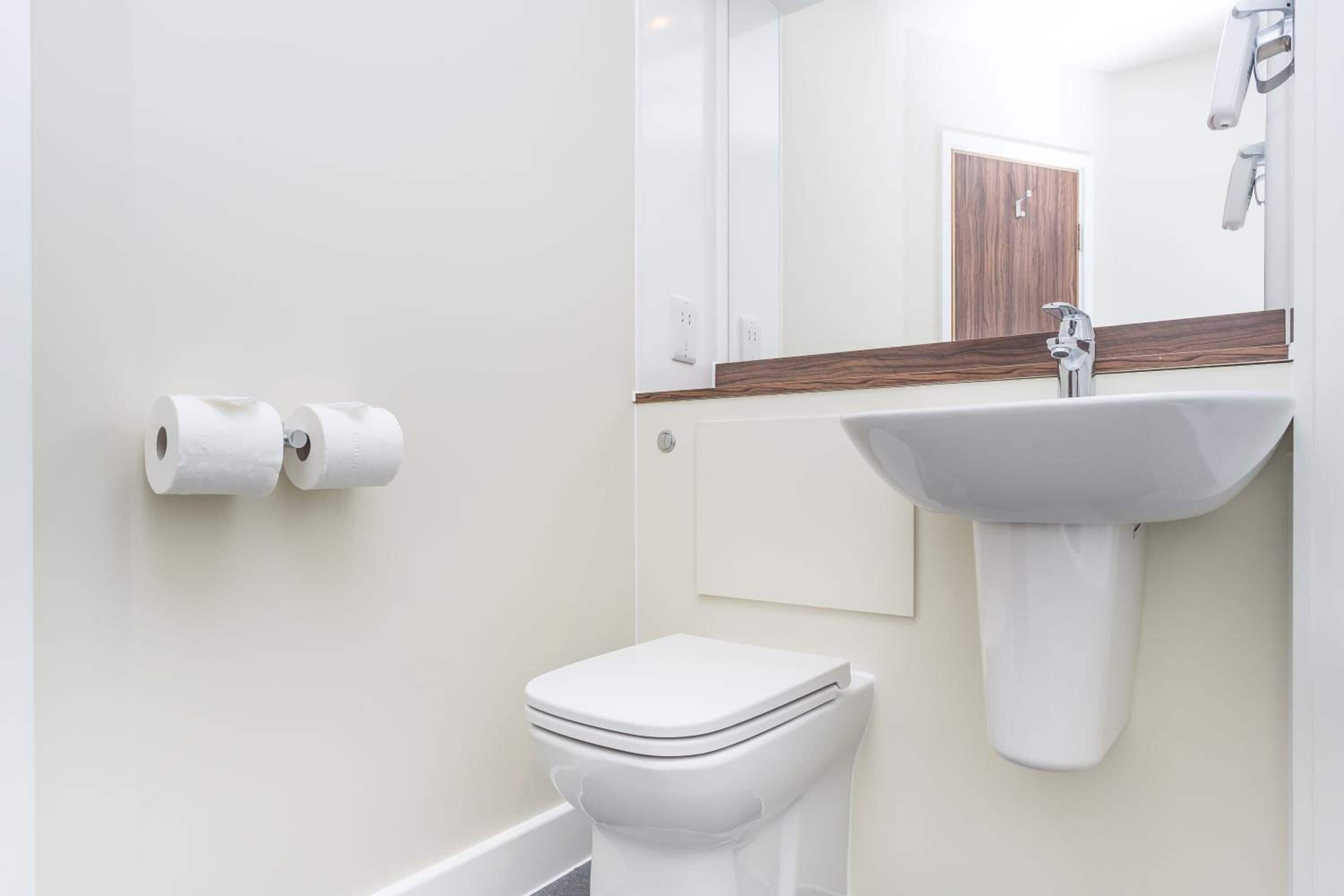 Uma casa de banho moderna com sanita, lavatório e dois rolos de papel higiénico na parede.