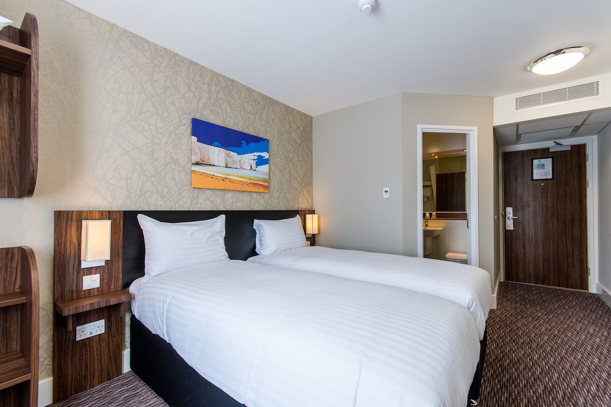 A hotel room with a large bed, a nightstand, a wall-mounted painting, and a door leading to a bathroom.