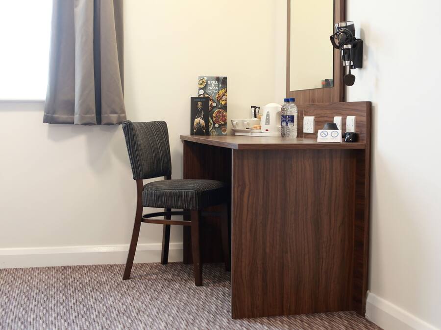 A small, private office area with a wooden desk, a chair, a mirror, a kettle, a water bottle, and a microwave.