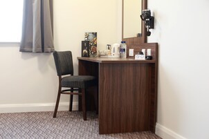 Un espacio de oficina pequeño y privado con un escritorio de madera, una silla, un espejo, un hervidor, una botella de agua y un microondas.