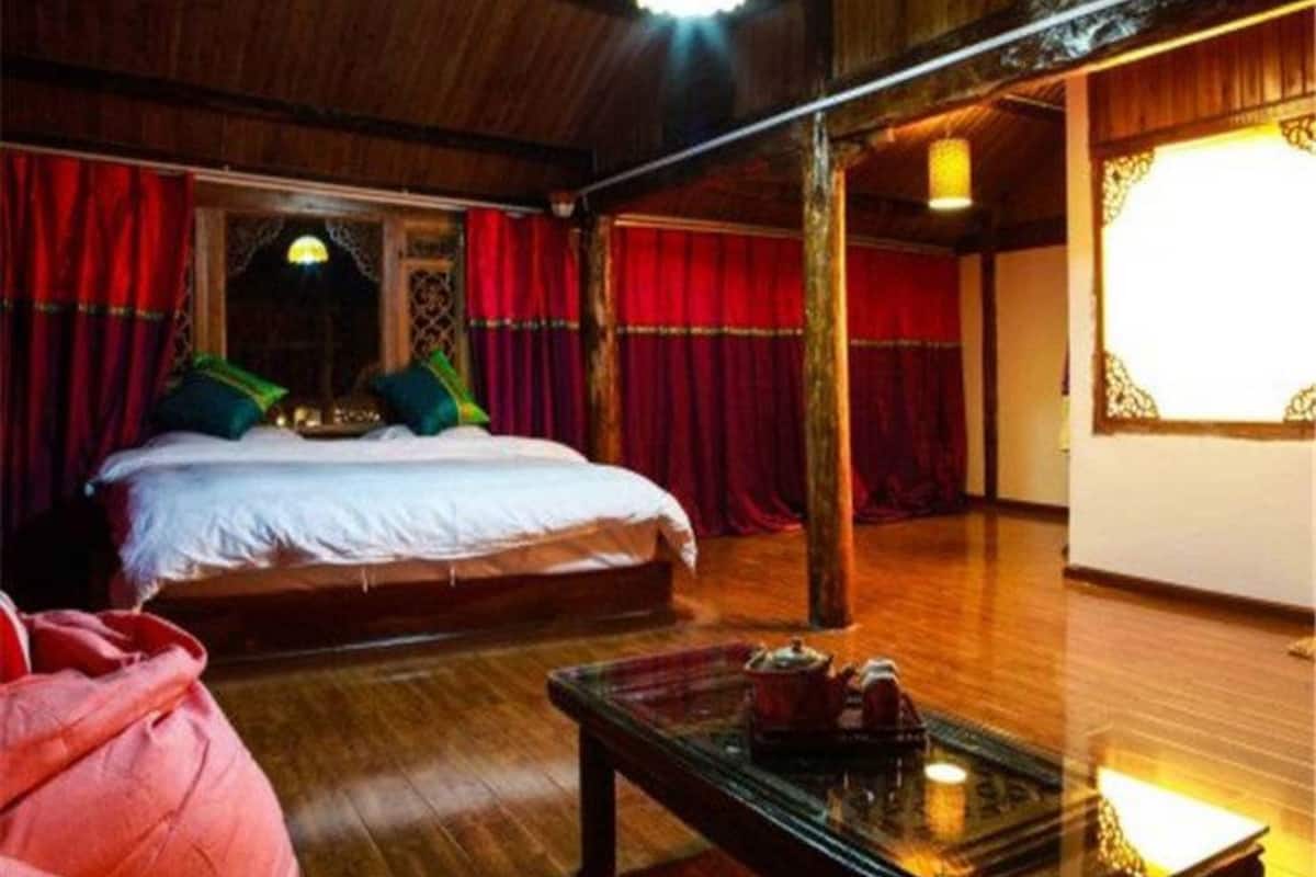 A traditional room with a wooden floor, a bed with red curtains, and a table with a teapot.