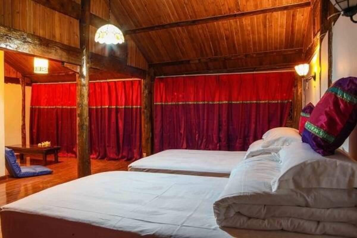 A room with wooden beams, a bed with white bedding, a red curtain, and a small table with a chair.