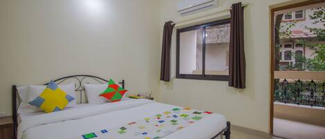 A bedroom with a bed, an air conditioner, a window with curtains, and a view of a building outside.