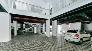 A spacious indoor parking area with a checkered floor, a white car, and a staircase leading to a mezzanine level. - OYO 16140 Home Exotic 1BHK Kakkanad (Kanayannur)