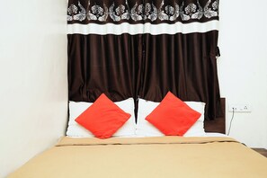 A bed with a beige bedspread, two red pillows, and a black and white patterned curtain. - The Pearl Inn (Pune)